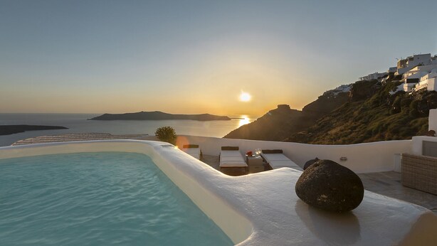 Ein Poolbereich mit Blick auf den Sonnenuntergang über dem Meer, eine Liege und ein Felsen.