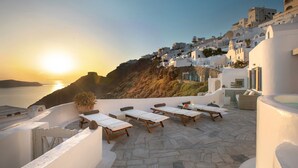 Eine Terrasse mit Liegestühlen mit Blick auf die Küste bei Sonnenuntergang.
