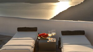 Blick auf das Meer mit zwei Liegestühlen, einem Teller mit Wassermelone und zwei Weingläsern.