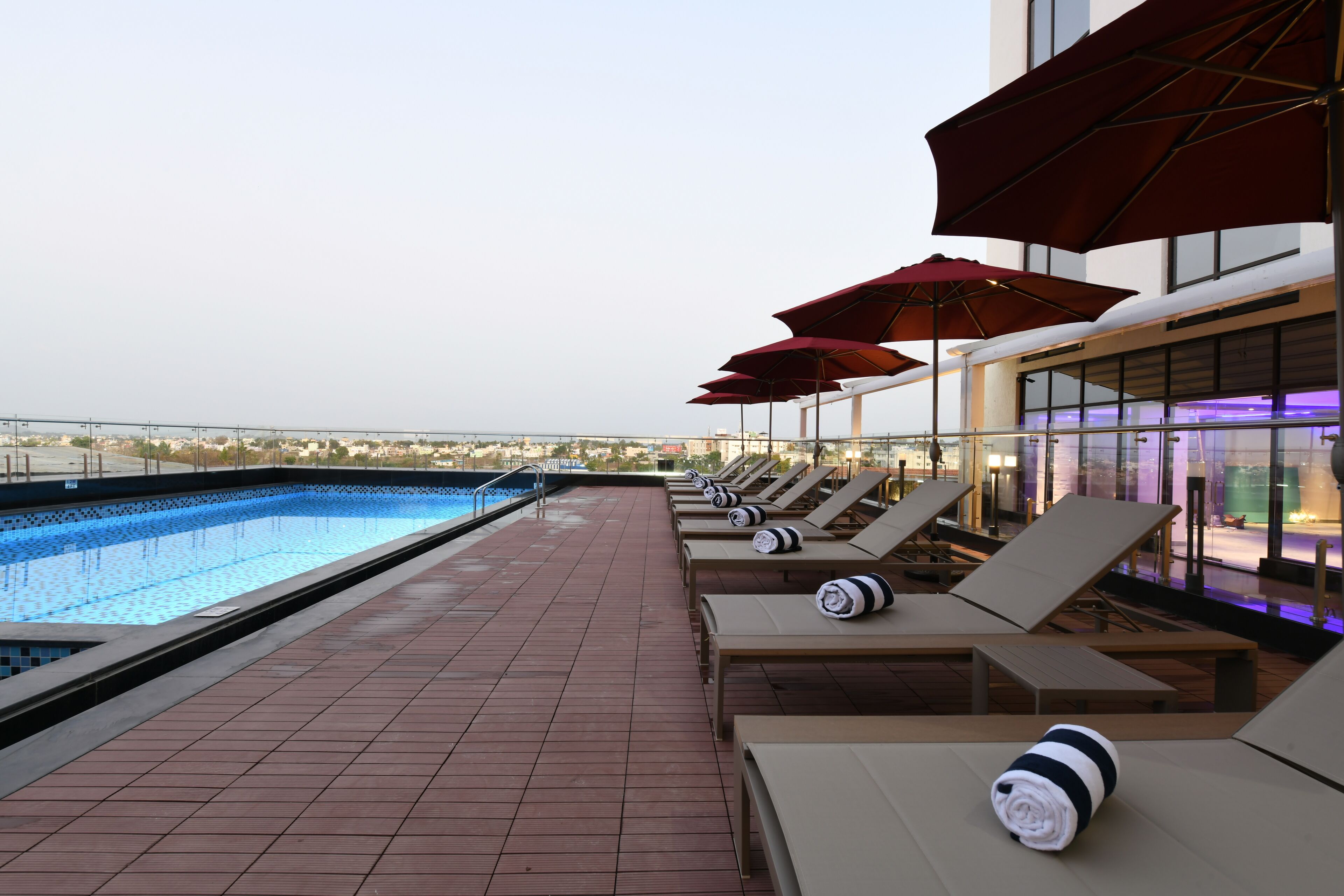 A rooftop pool area with lounge chairs and umbrellas, a swimming pool, and a view of the cityscape.