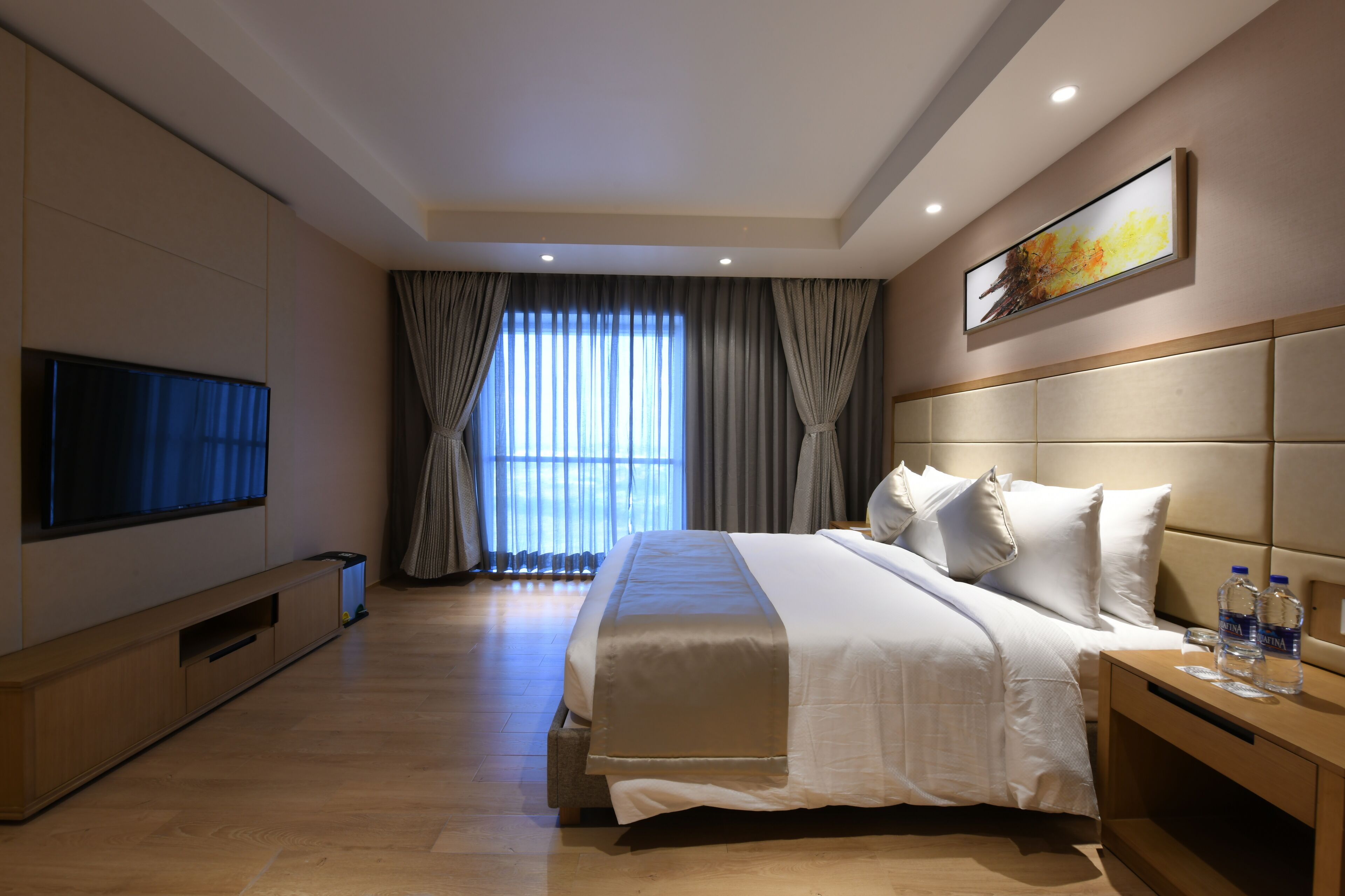 A modern hotel room with a large bed, a flat-screen TV, and a window with curtains.