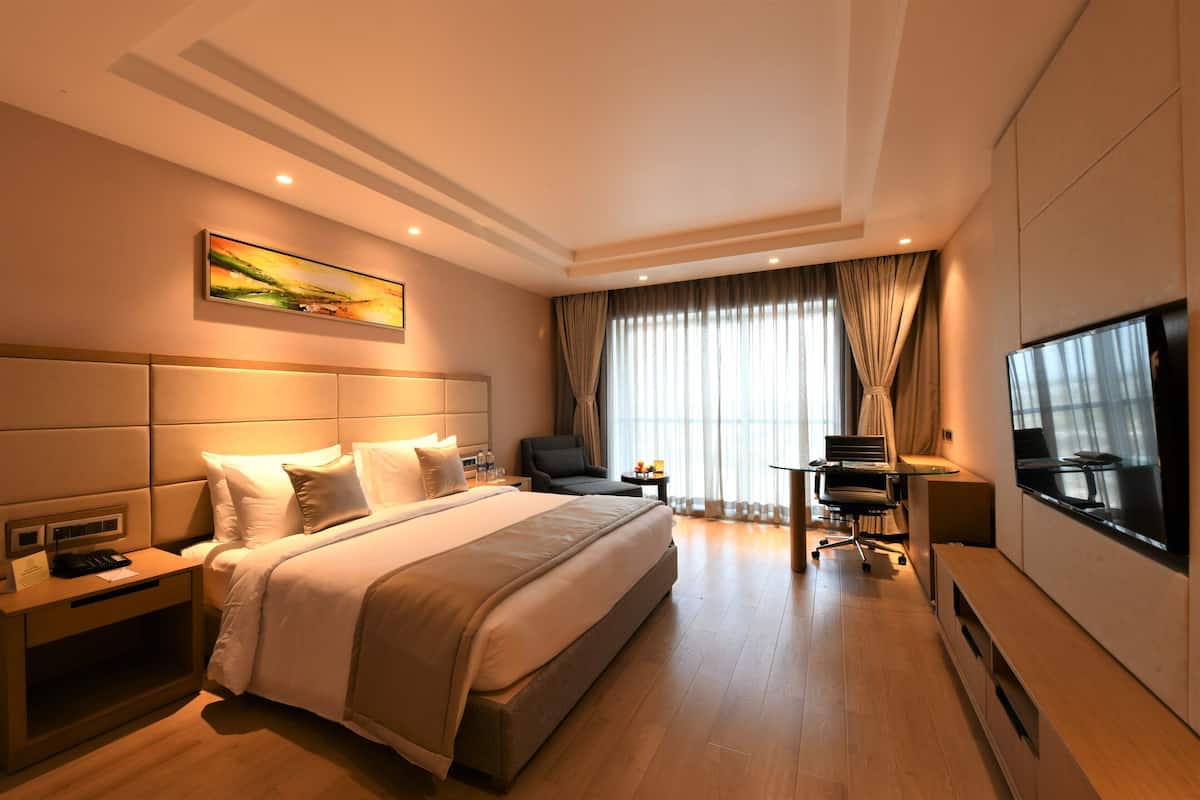 A modern hotel room with a large bed, a desk, a chair, a TV, and a window with curtains.