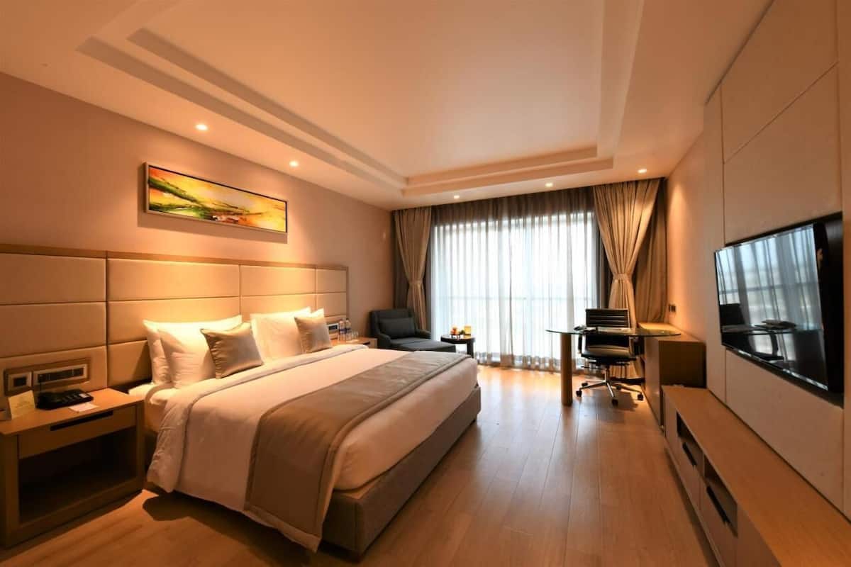 A hotel room with a large bed, a desk, a chair, a TV, and a window with curtains.