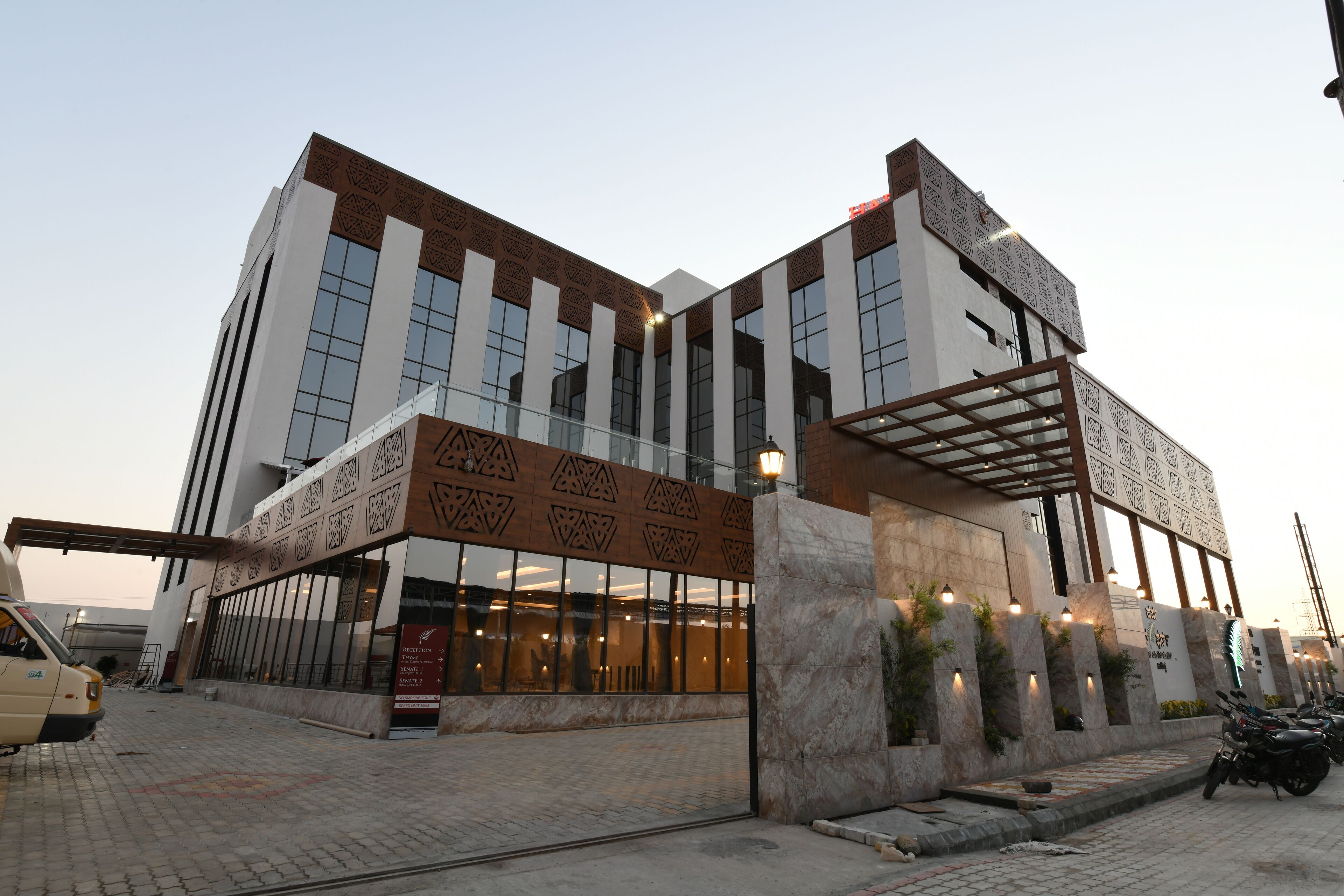 A modern building with a glass facade, a reception area, and a parking lot with motorcycles.