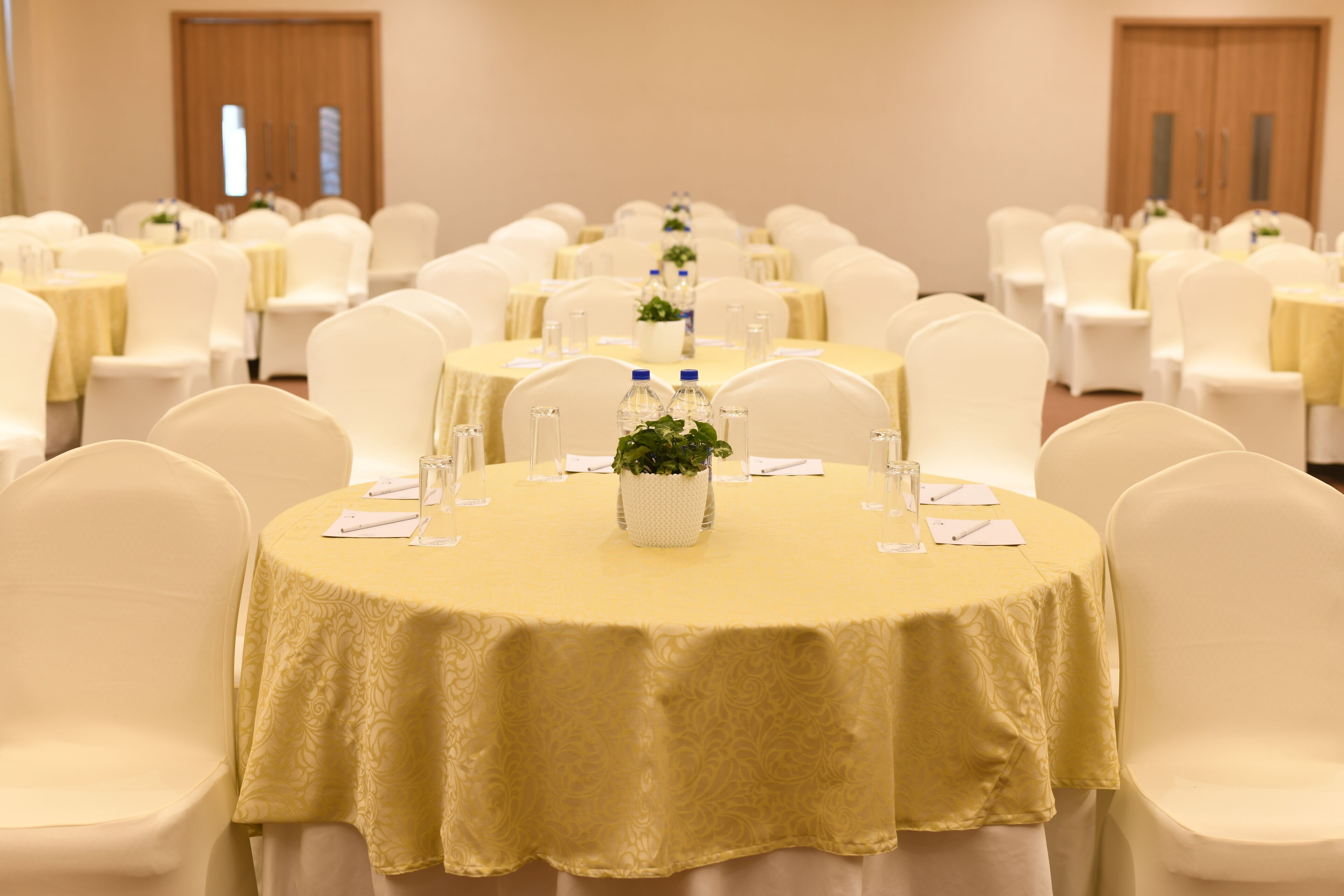 Une salle de banquet avec des tables rondes recouvertes de nappes jaunes, des chaises blanches et de petits centres de table.