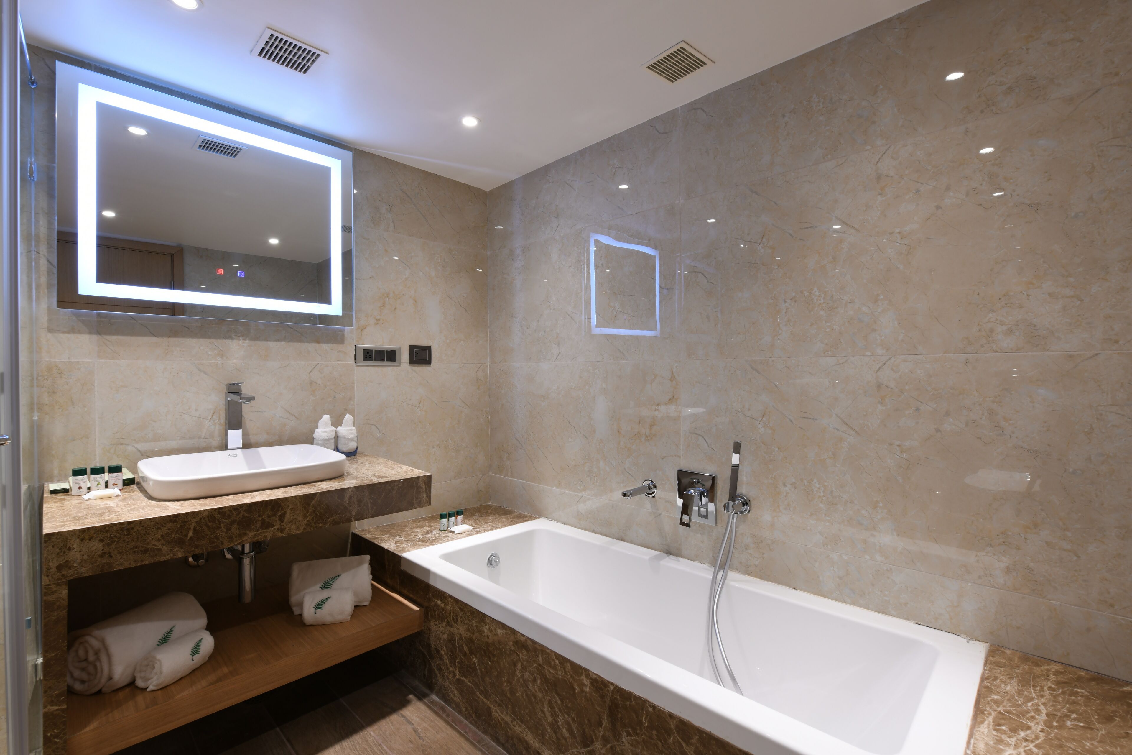 A modern bathroom with a large mirror, a sink, a bathtub, and a vanity with a towel rack.