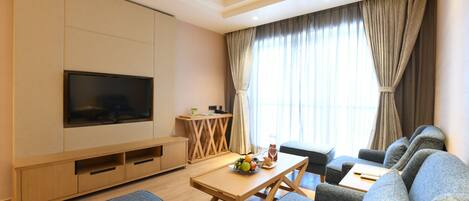 Una sala de estar moderna con un televisor de pantalla plana, sofás grises, una mesa de centro de madera y una pequeña mesa de comedor.