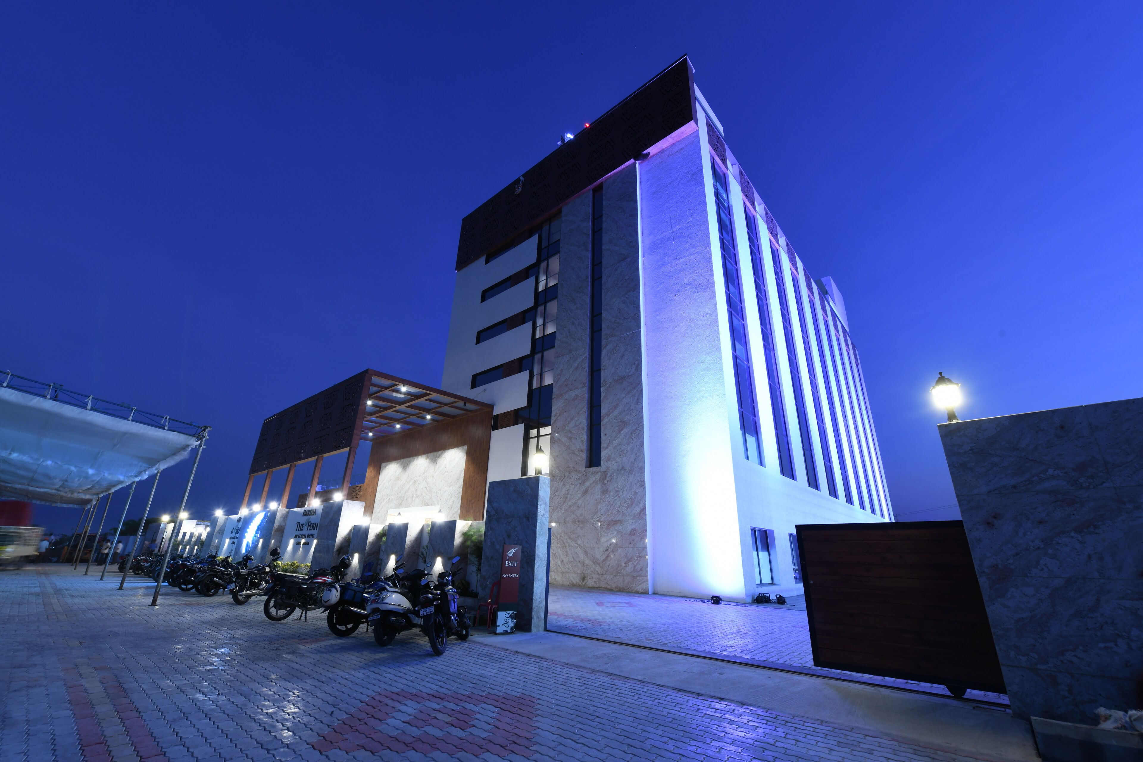 A modern building with a prominent entrance, a covered parking area with motorcycles, and a well-lit facade.