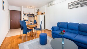 Una sala de estar moderna con un sofá azul, una zona de comedor con mesa y sillas, y una cocina al fondo.