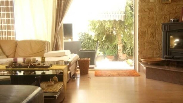 Una sala de estar con un sofá, una mesa de centro y una chimenea. Hay una ventana con cortinas y vistas al exterior con vegetación.