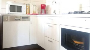 Una cocina con armarios blancos, microondas, cafetera y horno.