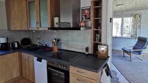 Una cocina compacta con armarios de madera, un horno empotrado y un lavamanos. Hay una pequeña zona de comedor con una silla y una mesa.