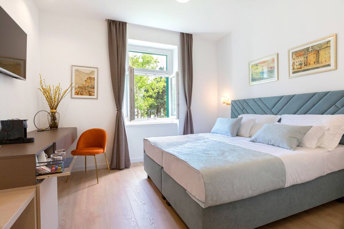 A bedroom with a bed, a desk, a chair, and a window with curtains.