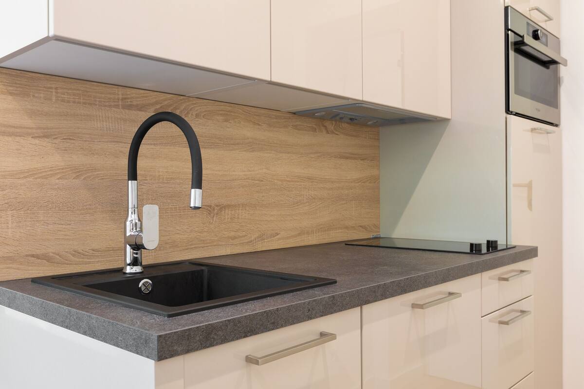A modern kitchen with a black sink, stainless steel faucet, and wooden backsplash.