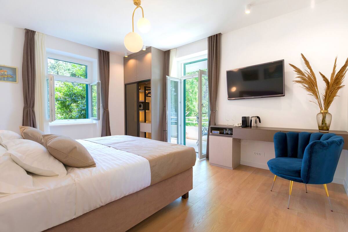 A modern bedroom with a bed, a desk, and a chair. There is a TV on the wall and a window with curtains.