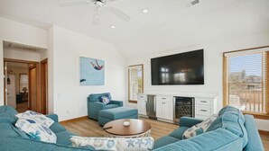 Una sala de estar con un televisor de pantalla plana grande, sofás color turquesa, una mesa de centro y una chimenea.