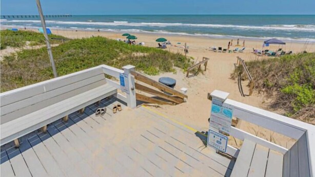 Vista a la playa desde una terraza de madera, con un banco, un basurero y una garita de salvavidas.
