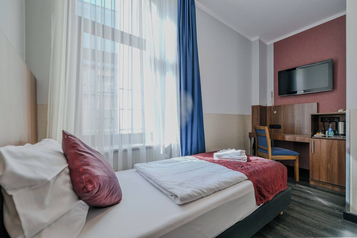 A hotel room with a bed, a desk, a chair, a television, and a window with curtains.