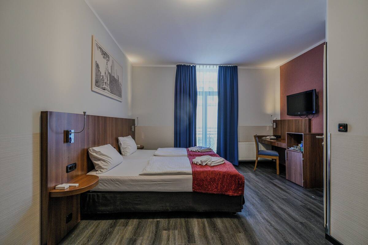 A hotel room with a bed, a desk, a chair, a television, and a window with curtains.