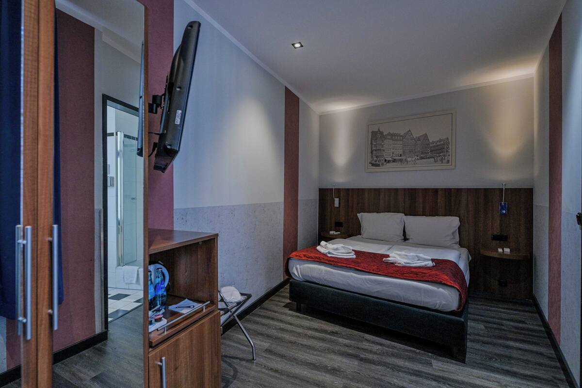 A hotel room with a bed, a TV mounted on the wall, a wooden cabinet, and a framed picture on the wall.