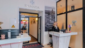 A reception desk with a nameplate, a clock, and a cityscape poster. - Ramada by Wyndham Frankfurt Central Station (Frankfurt)