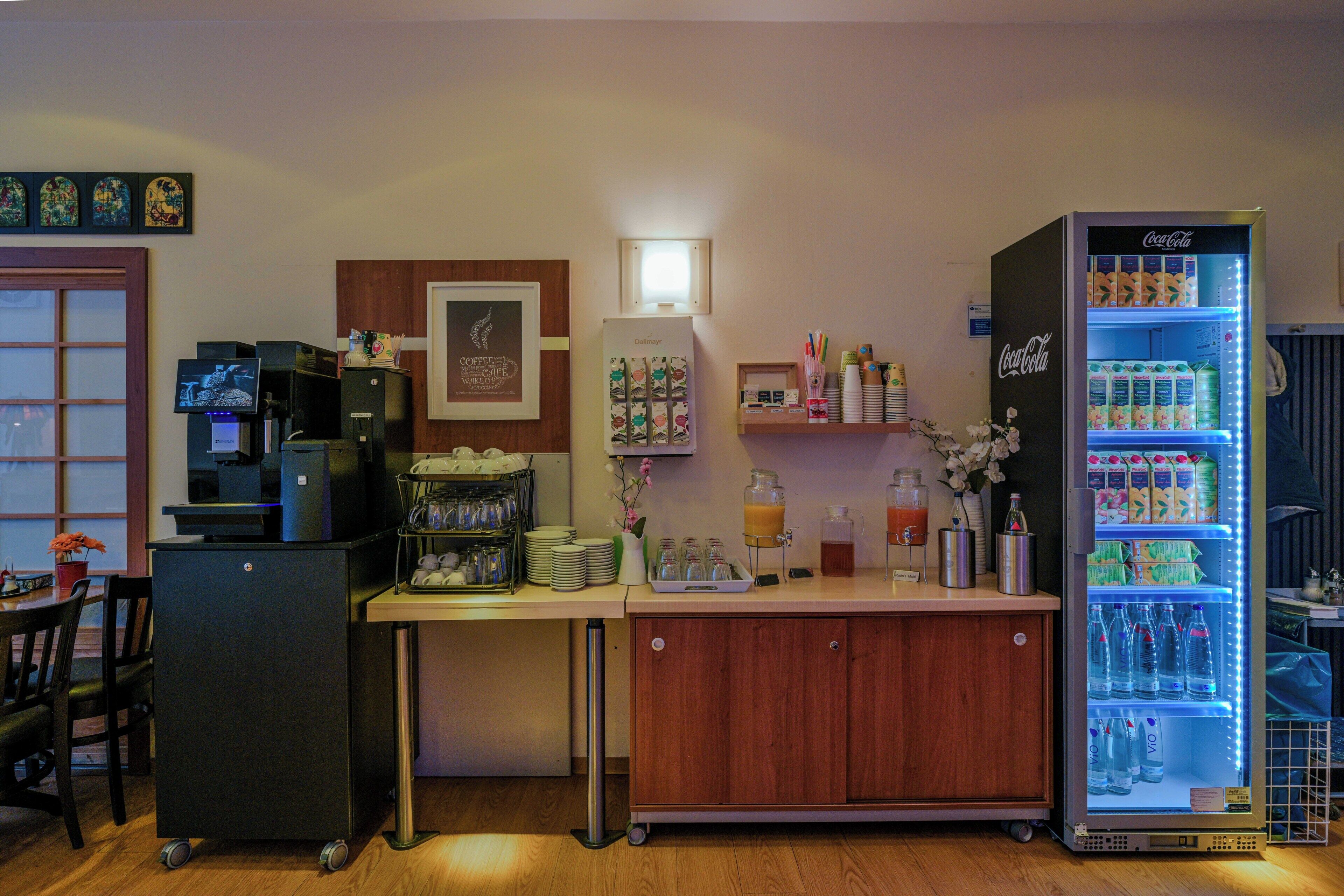 A kitchenette with a refrigerator, coffee machine, and a beverage dispenser.