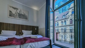 A hotel room with a bed, a framed picture on the wall, and a view of buildings through a window. - Ramada by Wyndham Frankfurt Central Station (Frankfurt)