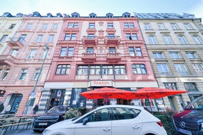 Un edificio de varios pisos con un llamativo letrero 'RAMADA', que presenta un estilo arquitectónico clásico con balcones ornamentados y ventanas grandes.
