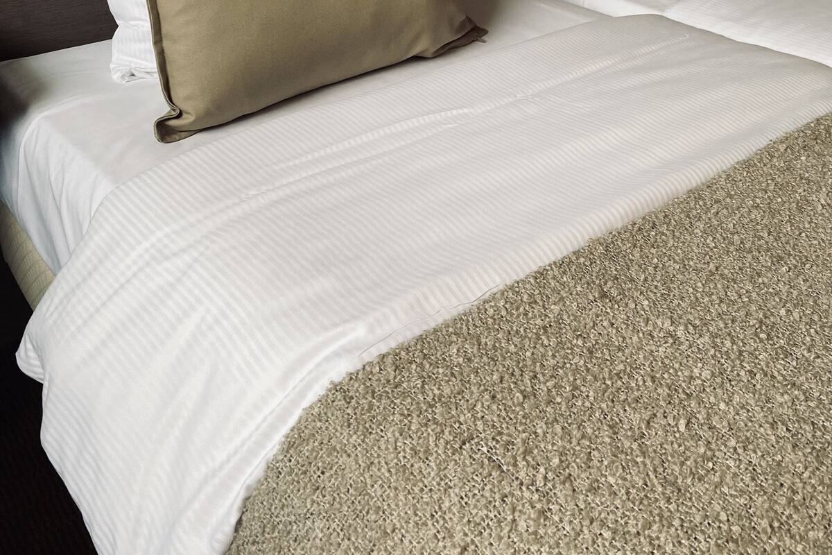 Habitación de hotel con dos camas, cada una con ropa blanca y una manta color beige.