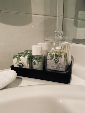 A bathroom shelf with toiletry items including a body lotion, soap, and a glass jar with a spoon. - Hotel Bornem (Bornem)