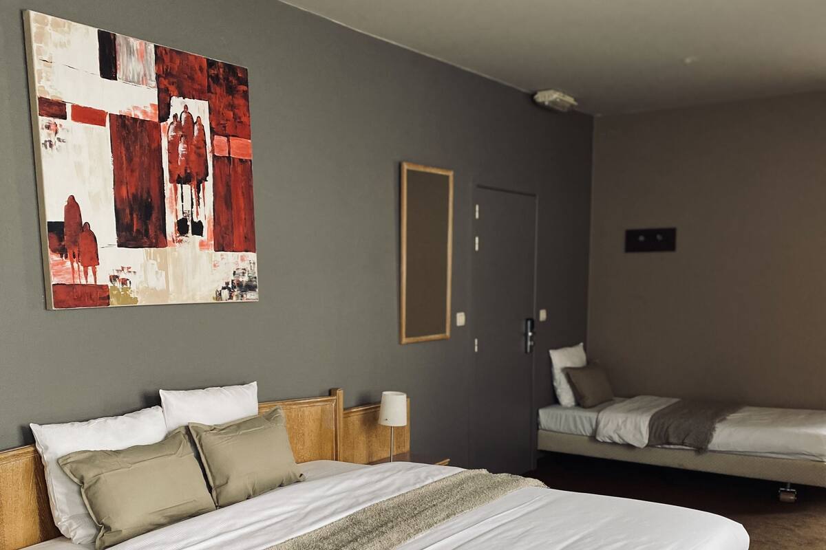 Una habitación de hotel con una cama grande, una cama más pequeña, un cuadro en la pared y una puerta.
