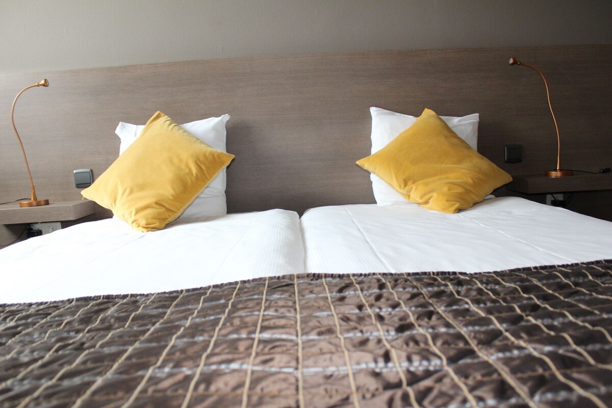 A neatly made bed with a patterned bedspread, two bedside tables with lamps, and a wooden headboard.