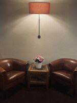 Una habitación con dos sillones de cuero, una mesita de madera con un florero y una lámpara de pie.