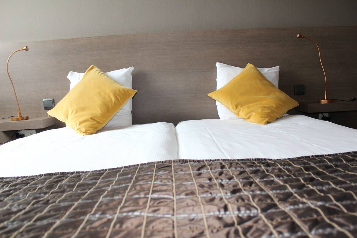 Una cama bien hecha con una colcha estampada, dos mesitas de noche con lámparas y un cabecero de madera.