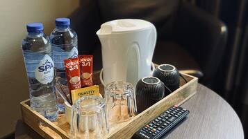 A tray with a water bottle, a coffee maker, a remote control, and a small container of coffee on a round table.