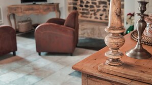 A wooden table with a decorative backrest, a stone wall, a television on a wooden stand, and a pair of red armchairs. - On a 3h property, in the heart of the forest, the gites du lety await you. (Perret)