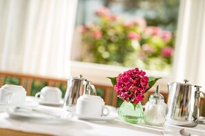 Ein Tisch ist gedeckt mit weißen Tassen und Untertassen, einer silbernen Teekanne, einem Glasbehälter und einer Vase mit rosa Blumen.
