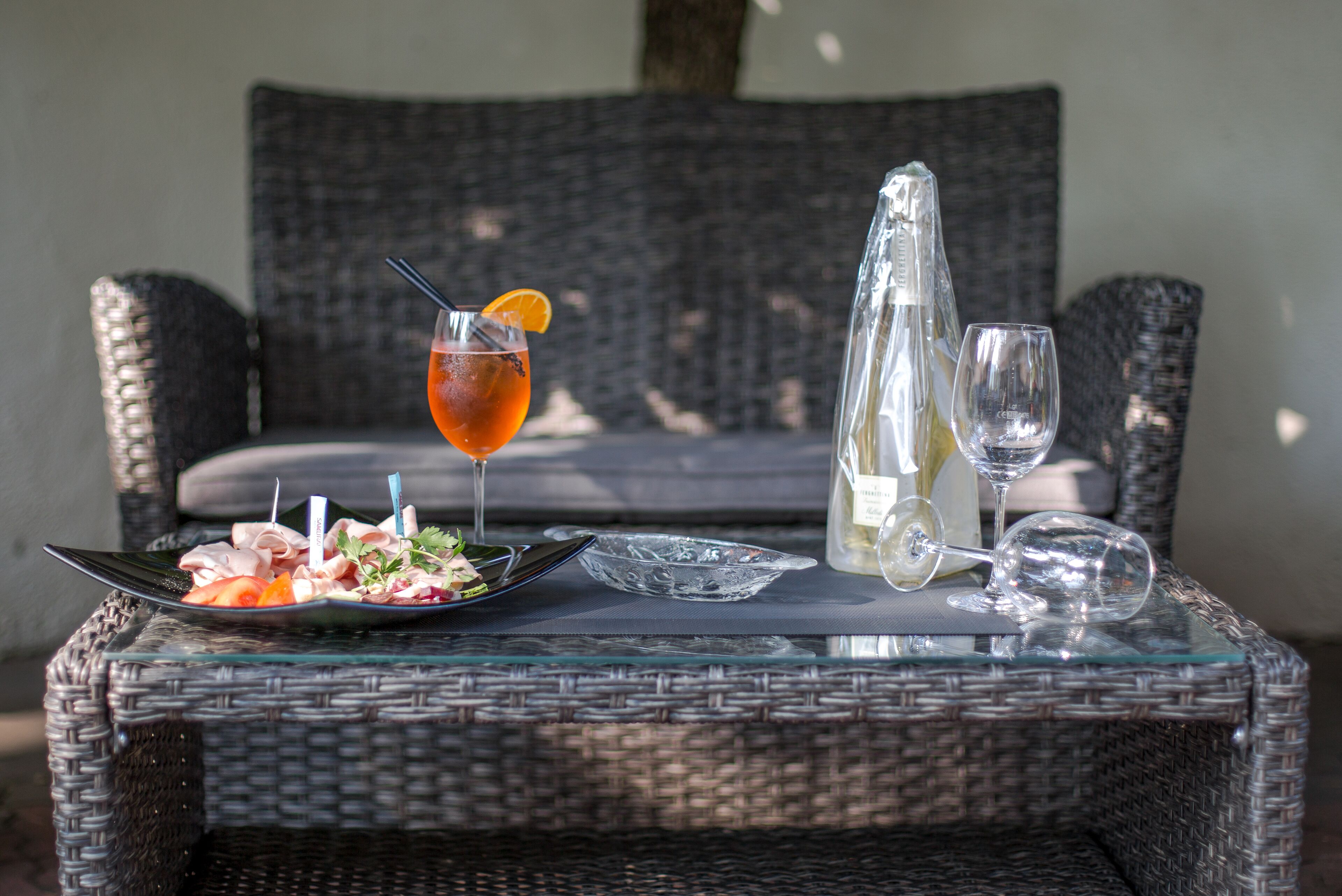 A wicker table with a plate of food, a glass of drink, and a bottle of water.