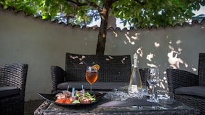 A table set outdoors with wicker furniture, a bottle of white wine, and a glass of red wine with an orange slice. - Hotel Heide Park (Ora)