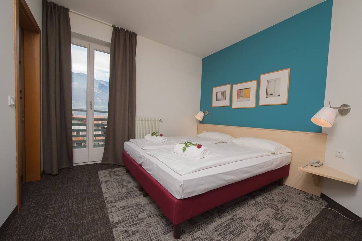 A hotel room with a bed, a view through a door, a blue accent wall, and a small bedside table.