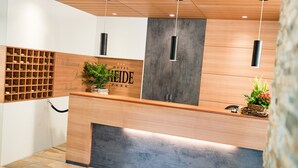 A hotel reception desk with a wooden counter, a plant, and a wall-mounted wine rack. - Hotel Heide Park (Ora)