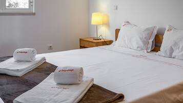Una habitación de hotel con una cama bien hecha, dos toallas blancas con la marca 'hopstays', una lámpara de noche y una ventana con vistas a árboles.