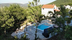 A villa with a swimming pool surrounded by trees, a patio with outdoor furniture, and a view of the hills. - Holiday Home Jadrić  (Dicmo)