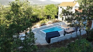 A swimming pool with a wooden deck and a table, surrounded by trees and a view of distant mountains. - Holiday Home Jadrić  (Dicmo)