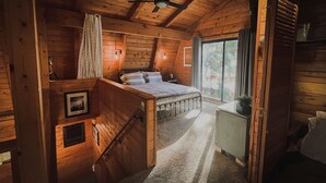 A wooden cabin bedroom with a bed, a ceiling fan, a window with curtains, and a small bedside table. - State 48 Retreat Prescott Arizona (Prescott)