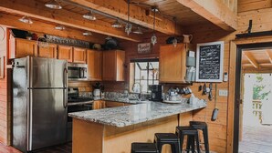 A kitchen with wooden cabinets, a stainless steel refrigerator, a granite countertop, and bar stools. - State 48 Retreat Prescott Arizona (Prescott)