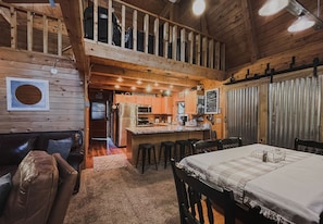 Cozy cabin-style accommodation with a high ceiling, exposed beams, and a loft area above the kitchen.