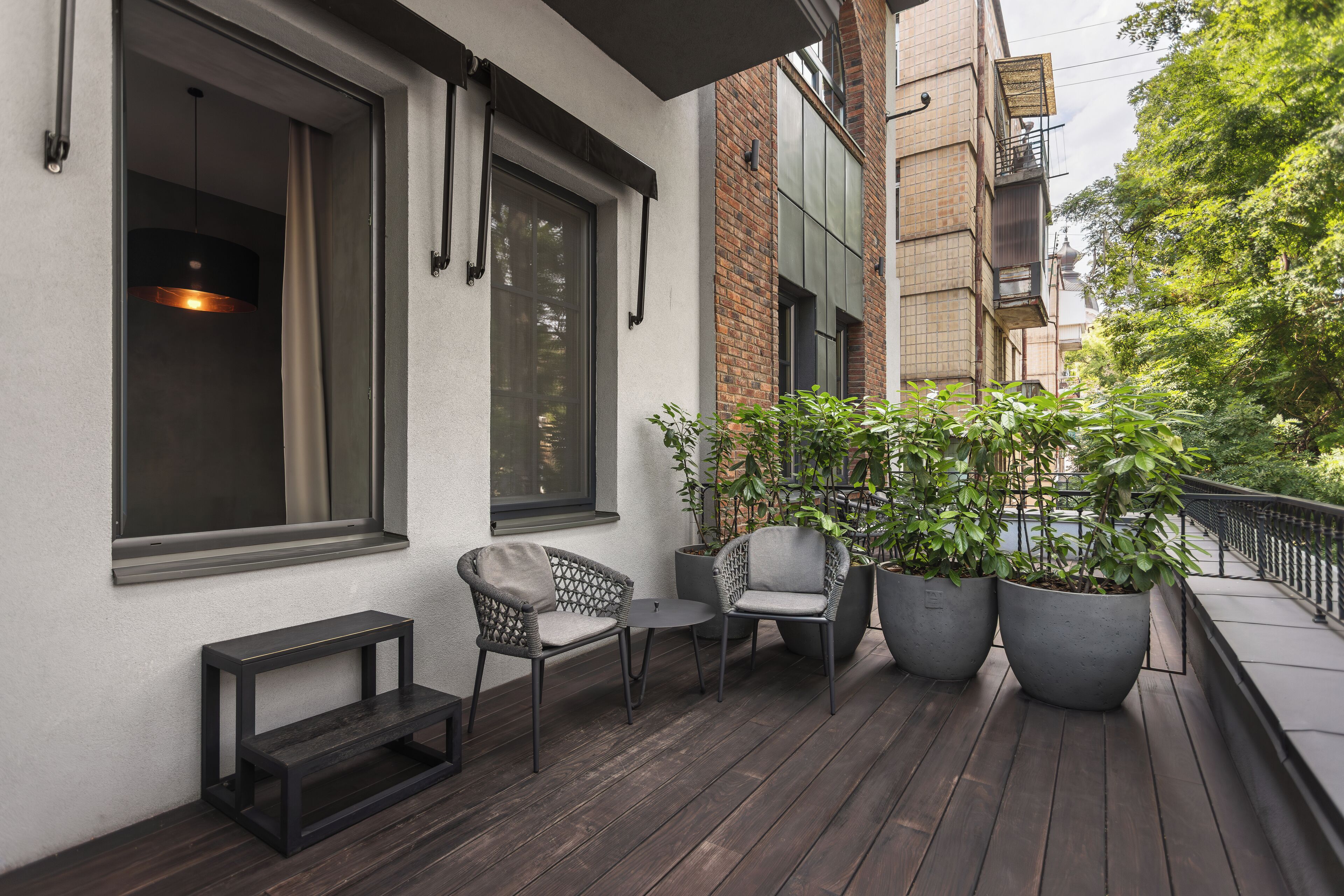 Een balkon met twee rieten stoelen, een klein tafeltje en twee grote potplanten.