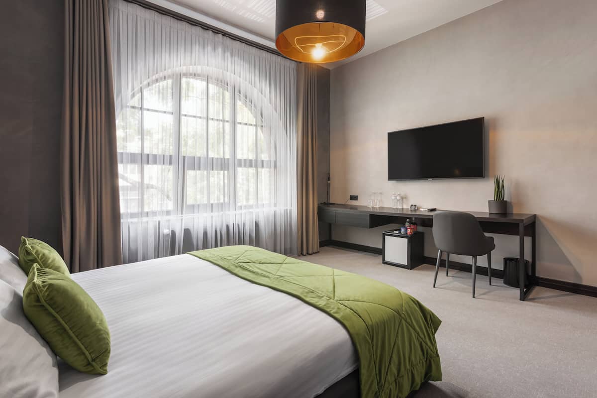 A modern hotel room with a large bed, a desk, and a TV.