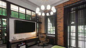 A hotel room with a large flat-screen TV, a desk with a chair, a bed with a green bedspread, and large windows with curtains. - BRYK Hotel (Odesa)